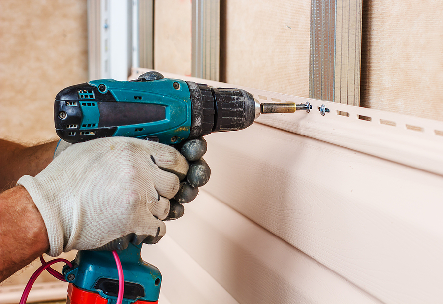 man screws in a wall using an electric screwdriver attaching siding to metal construction